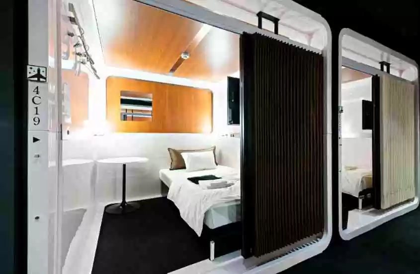 mesa redonda branca e travesseiros em cima de cama de solteiro branca, em um hotel cápsula em tokyo
