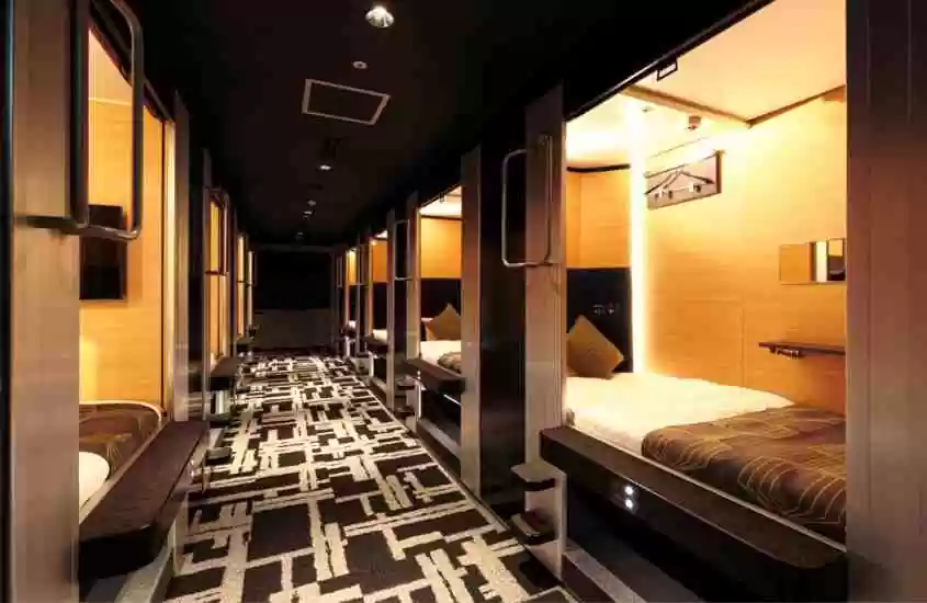 travesseiro preto, colchão branco, prateleira e espelho em acomodação com paredes de madeira em corredor cheio de cápsulas em hotel em tokyo