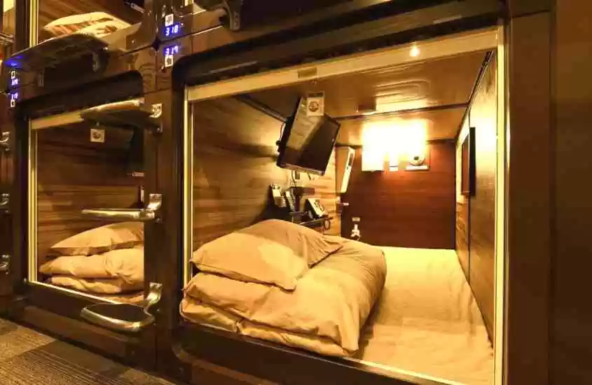 travesseiro, edredom, colchão de solteiro e TV em cápsula com paredes de madeira em hotel cápsula em tokyo