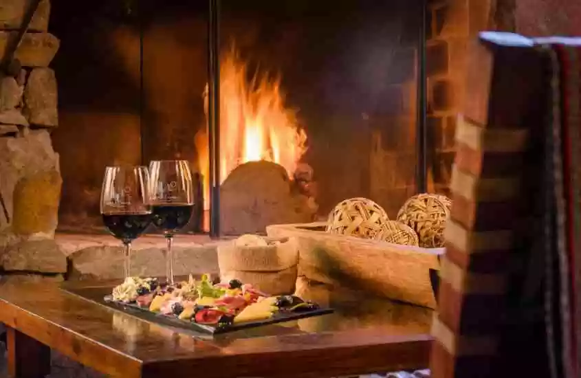taças de vinho e frios em cima de mesa de madeira, em frente a lareira em hotel vinícola em mendoza