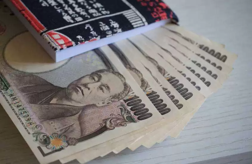 caderno preto e notas de iene em cima de mesa branca