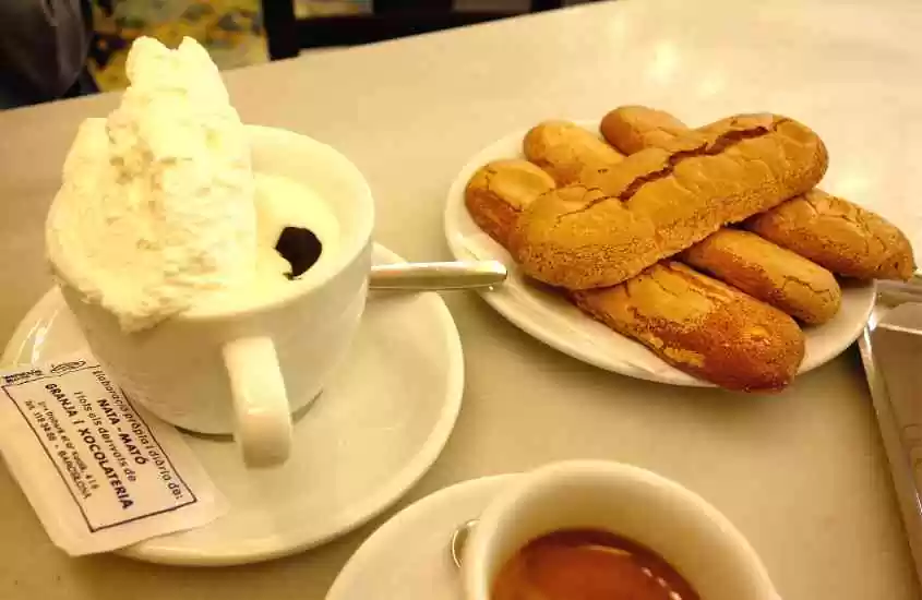xícara de café com chantilly e prato de churros em cima de mesa branca