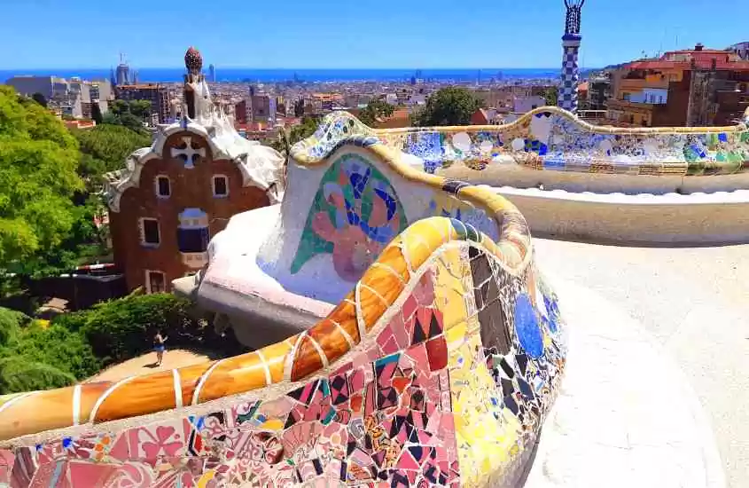 durante dia ensolarado, vista aérea de azulejos coloridos em parede branca , prédios e árvores em parque guell, ponto turístico em barcelona