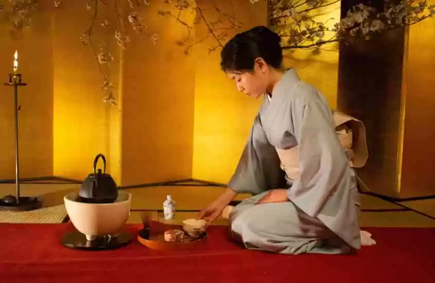 japonesa vestida com quimono cinza, arruma xícara no chão durante cerimônia do chá