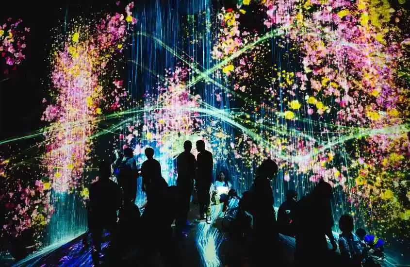 silhueta de pessoas em frente a tela iluminada que exibe diversas artes