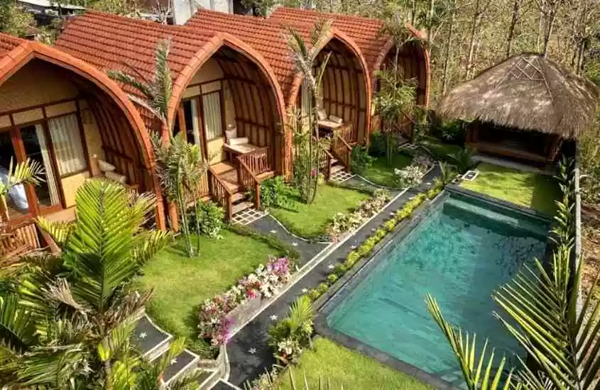 durante o dia, vista aérea de bangalôs de madeira e palha, em frente a jardim com piscina retangular