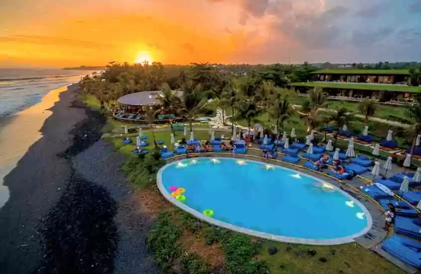 durante entardecer, vista aérea de diversas espreguiçadeiras ao redor de piscina redonda com vista para o mar em um dos hotéis de luxo em bali