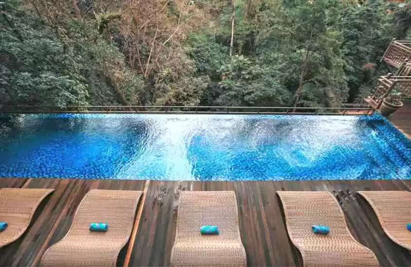 durante o dia, espreguiçadeira de palha em frente a piscina de borda infinita com vista para a floresta