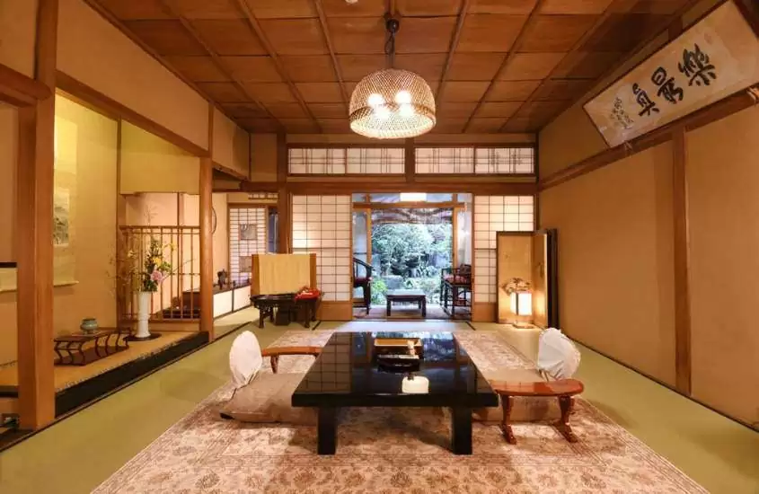 mesa retangular de madeira, almofadas e vaso com flores em sala de estar de ryokan