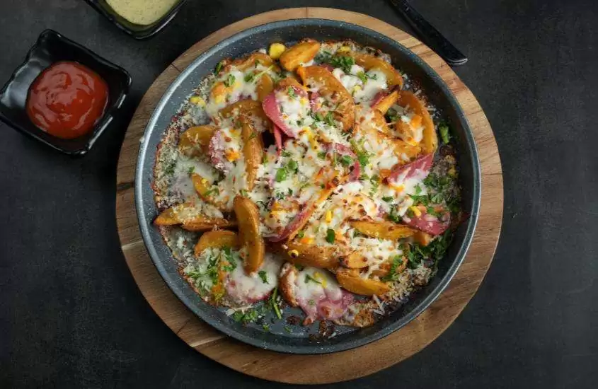 vista aérea de uma porção de paella, um prato típico da espanha feito com arroz, frutos do mar, frango e temperos, servida em uma vasilha preta redonda sobre uma mesa preta