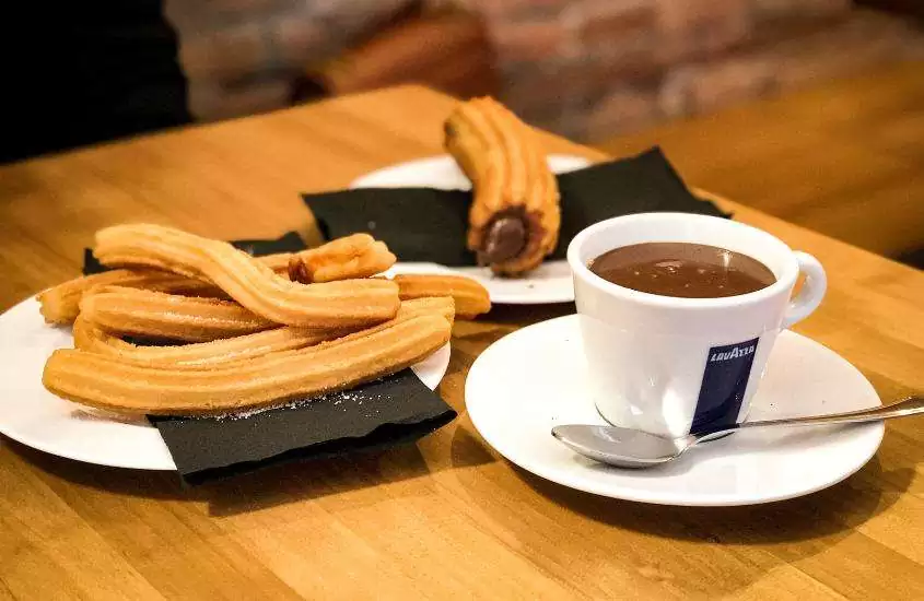 churros de chocolate e xícara de chocolate quente em cima de mesa de madeira