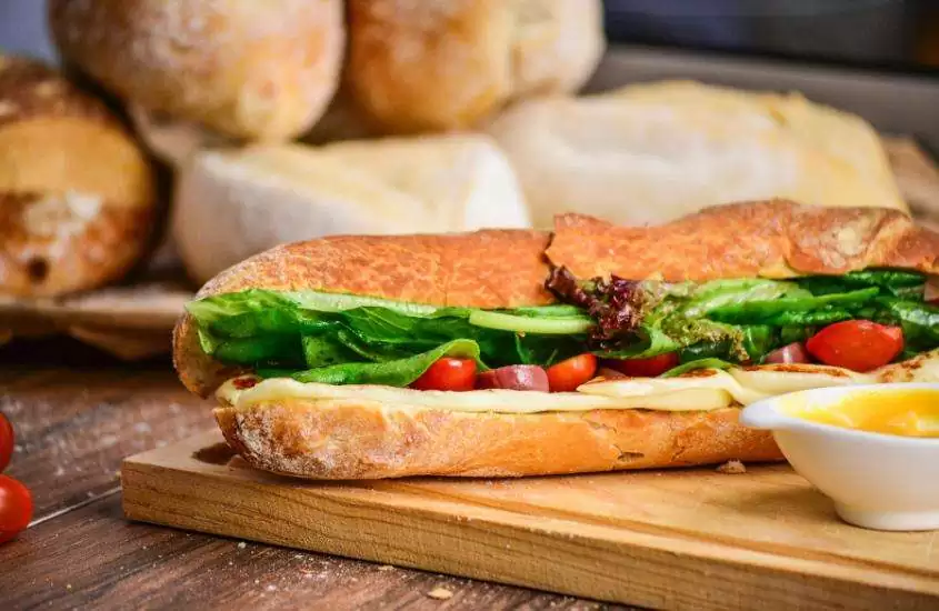 sanduíche com pão rústico, presunto, queijo, salame e vegetais em cima de mesa de madeira