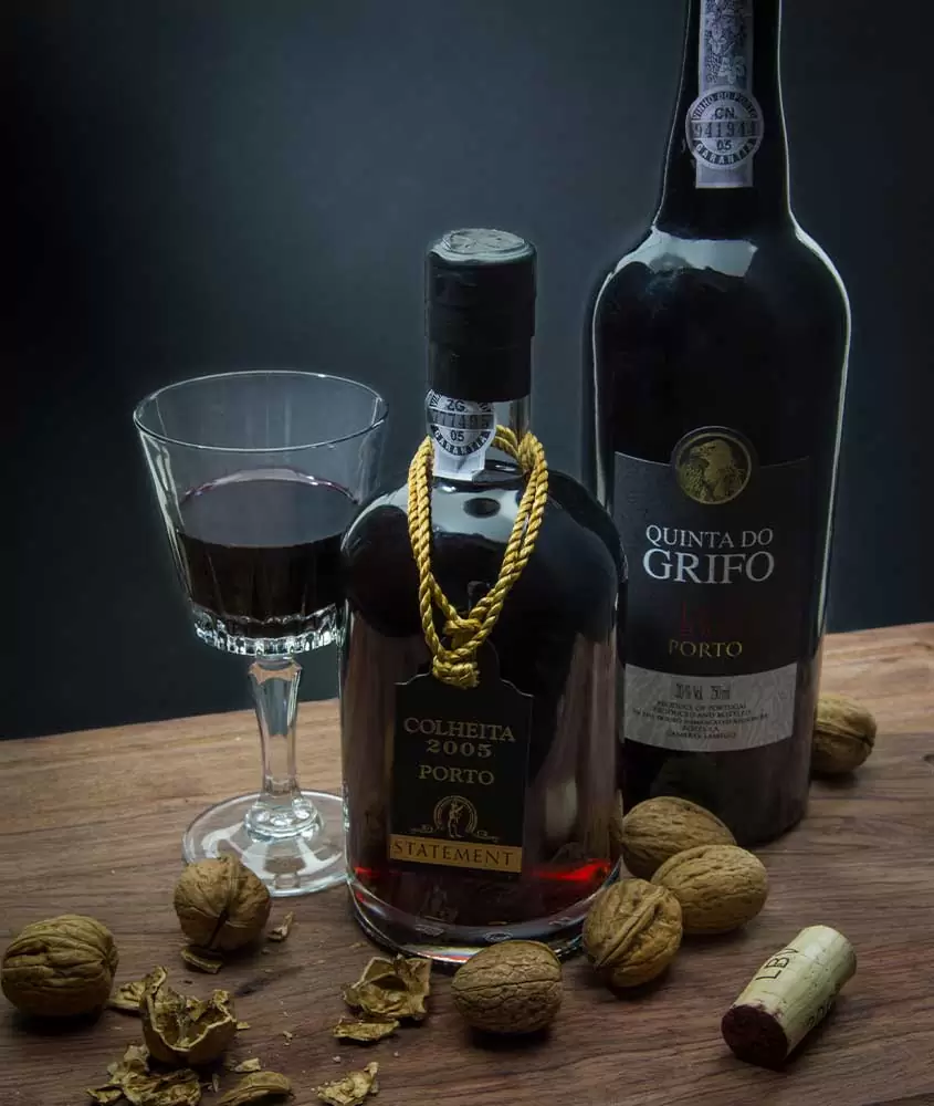 Taça de vinho tinto e duas garrafas de vinho do porto Quinta do Grifo, em cima de uma mesa de madeira escura