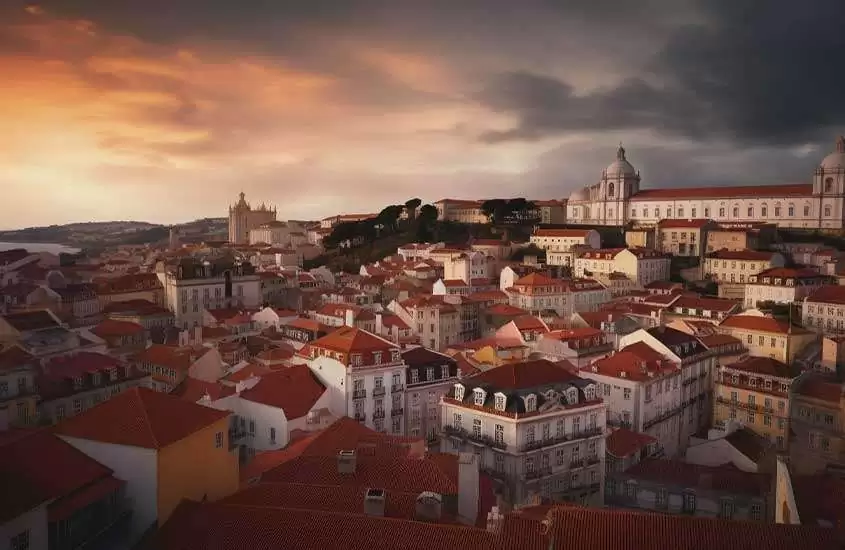 vista aérea e construções e prédios brancos com telhados laranjas, iluminados pela luz do entardecer, em portugal