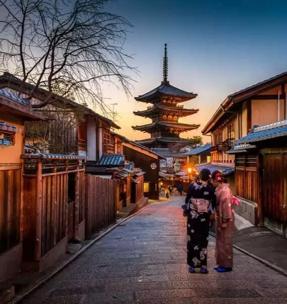 Duas gueixas, com suas tradicionais roupas japonesas, caminhando em uma rua de paralelepípedos de Kyoto durante o entardecer