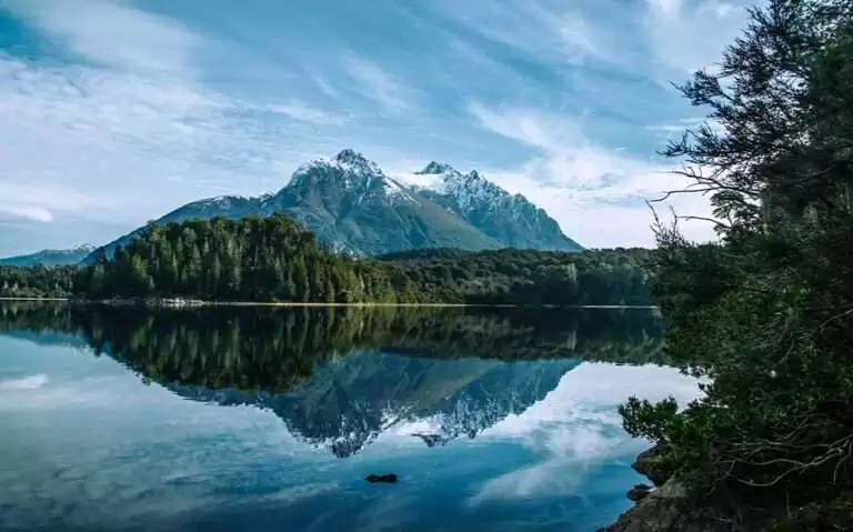 Durante o dia, paisagem de inverno em Bariloche com árvores cobertas de neve e montanhas nevadas refletidas em um lago cristalino
