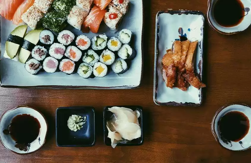 diversos sushis e molhos servidos em vasilhas brancas, dispostos em uma mesa de madeira