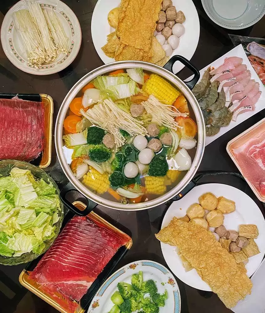 Vista de cima de mesa preta com panela quente no centro, com Shabu Shabu, prato da comida japonesa com fatias de carne, legumes, tofu e macarrão