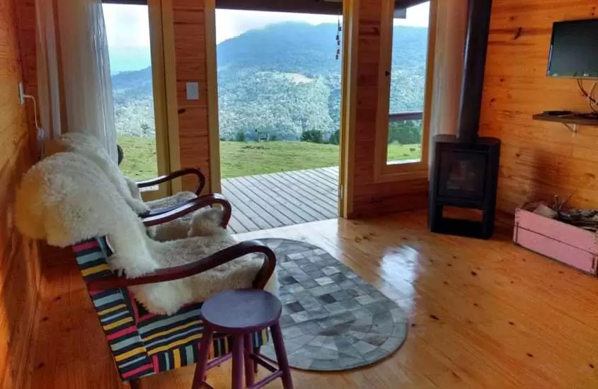 durante o dia, duas poltronas em frente a lareira em sala de estar de chalé da madeira com vista para as montanhas em Urubici