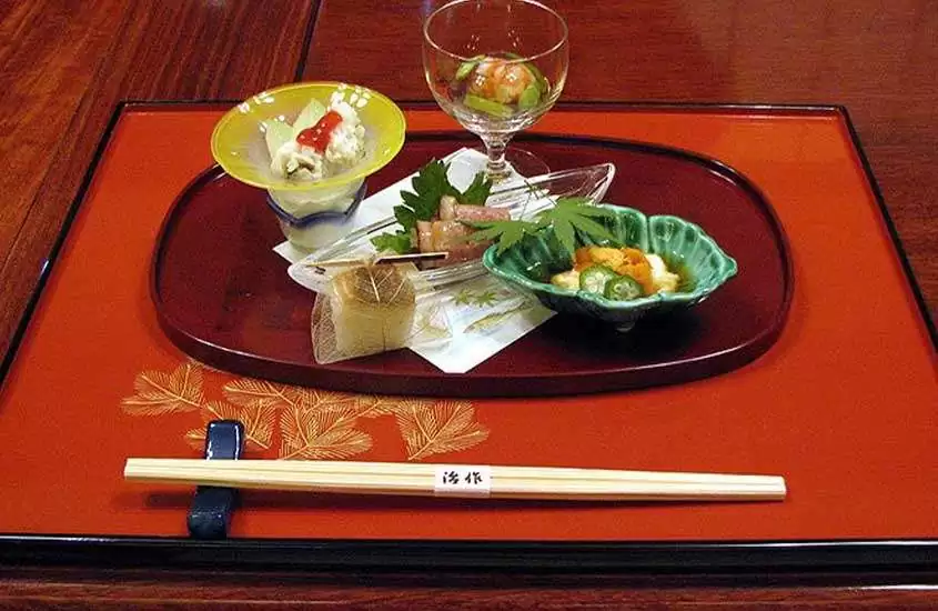 peixe cru, legumes e arroz servidos em pequenas tigelas, em cima de bandeja vermelha, junto com hashi