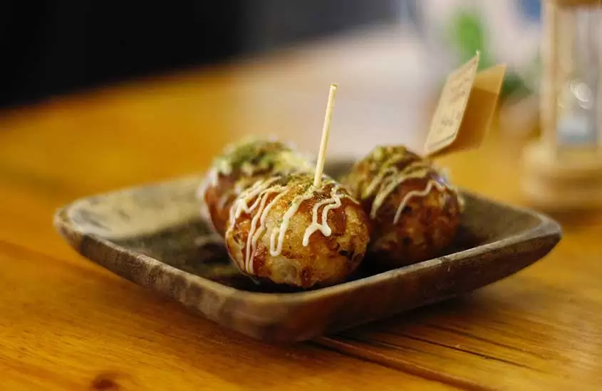 Takoyaki, uma iguaria japonesa com bolinhos de massa recheados com polvo picado, servidos em um prato quadrado cinza