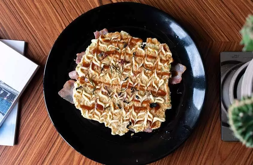 Okonomiyaki, prato típico japonês, à base de fairnha, água e ovos, servido em cima de uma mesa de madeira