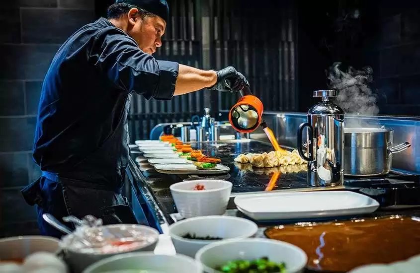 Grelhador de teppanyaki em ação em restaurante japonês, cozinhando pratos personalizados na chapa quente