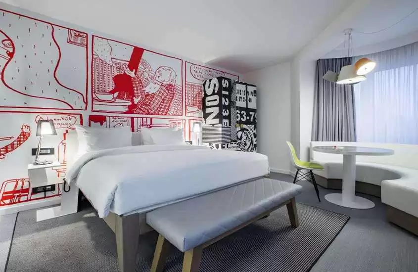 cama de casal, sofá, mesa e cadeira e suíte com paredes brancas com pinturas coloridas vermelhas