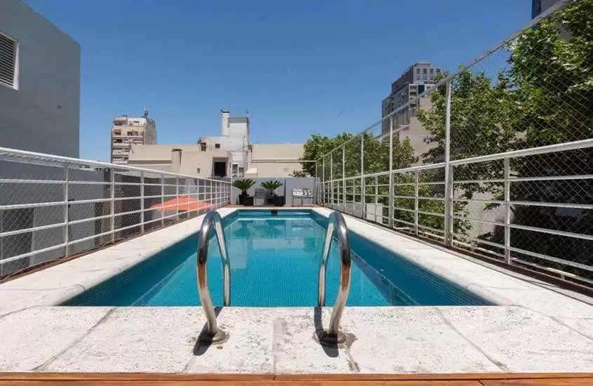 Durante um dia ensolarado, piscina retangular e espreguiçadeiras em área de lazer na cobertura de um hotel em buenos aires com vista para a cidade