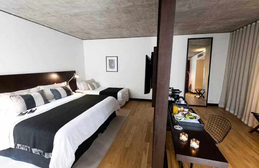 Suíte de hotel em Buenos Aires com duas camas de casal em frente à TV de tela plana. À direita, há uma mesa de jantar de madeira com uma taça de vidro sobre ela