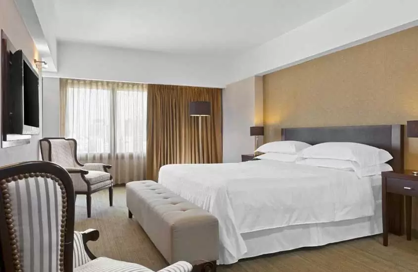 Durante o dia, duas poltronas com estampa listrada em frente a confortável cama de casal em suíte de hotel em Buenos Aires