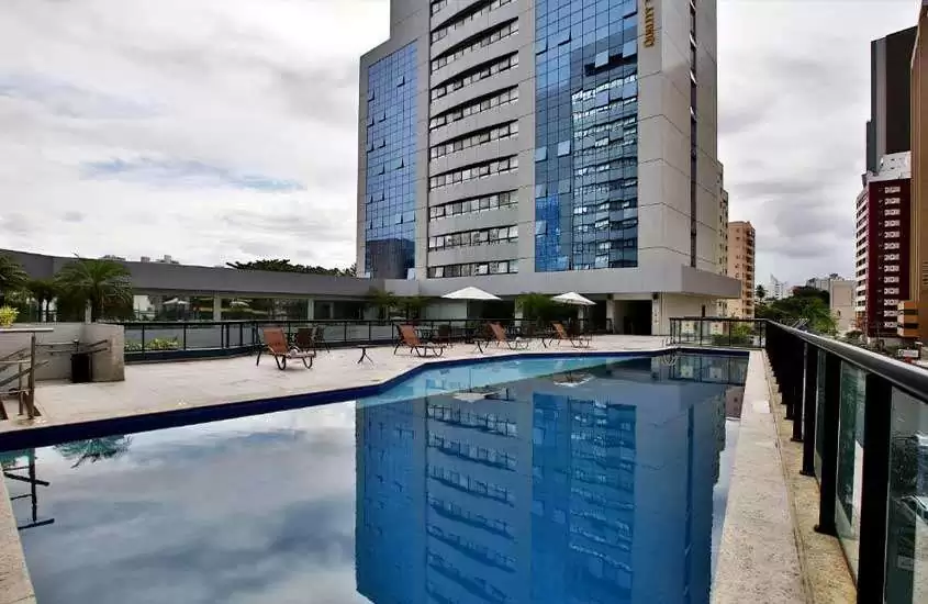 Durante um dia nublado, espreguiçadeiras e guarda-sóis em frente à piscina ao ar livre retangular de hotel em Salvador.