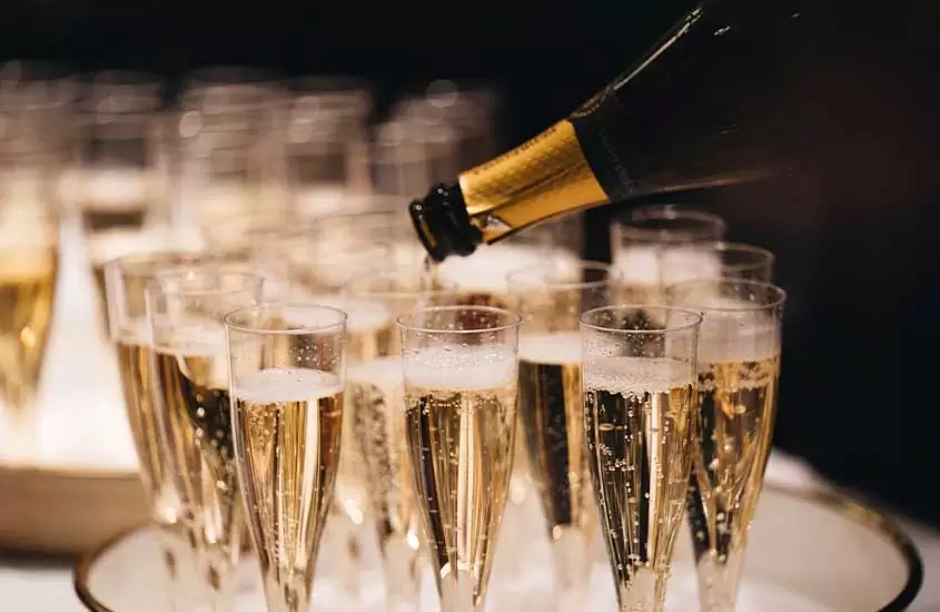 Uma garrafa de champanhe sendo despejada em taças de vidro na mesa de uma festa de réveillon em Salvador.