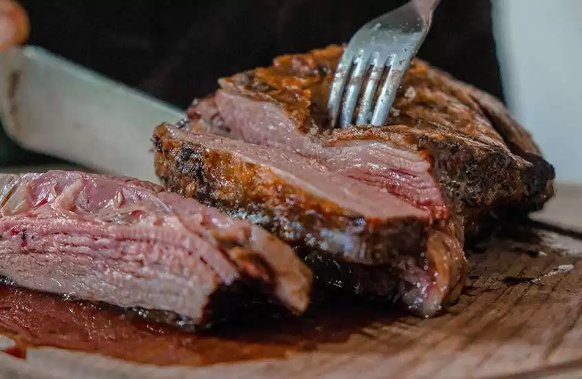 carne mal passada sendo cortada em uma tábua de madeira em um dos melhores restaurantes em bariloche