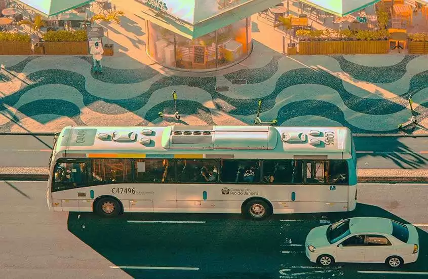 durante dia ensolarado, vista aérea de carro e ônibus brancos passando em avenida em frente a calçadão de copacabana