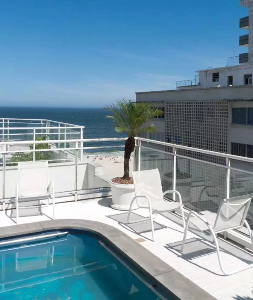 durante um dia ensolarado, cadeiras brancas em frente a piscina em cobertura de apartamento com vista para o mar