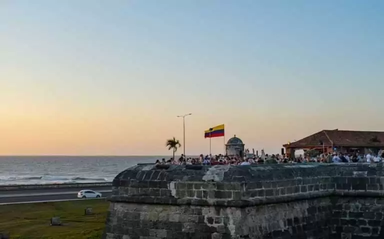 Mirante no interior da cidade murada de Cartagena, durante o entardecer, com uma animada multidão de pessoas apreciando a vista para o mar.