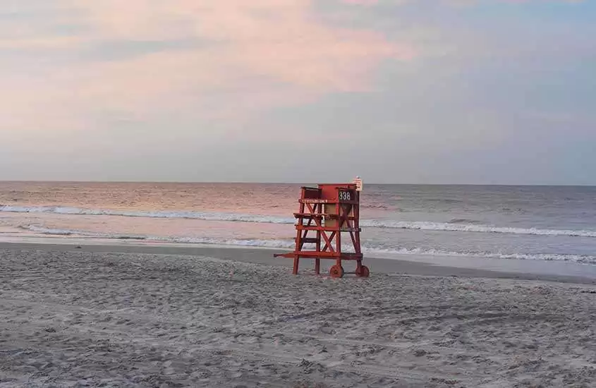 durante um entardecer, cadeira vermelha e alta de salva-vidas em areia de Daytona Beach, um dos lugares na flórida para conhecer.