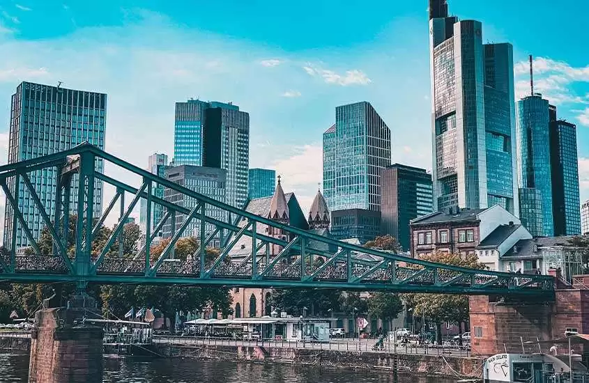 durante o dia, prédios às margens de rio Meno, onde há a Ponte de Ferro, um dos pontos turísticos em Frankfurt