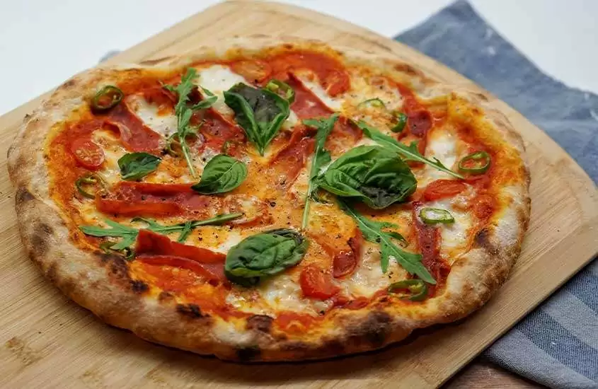 Pizza Margherita, um clássico da culinária italiana, servida em uma tábua de madeira, com uma combinação perfeita de queijo, tomate e manjericão