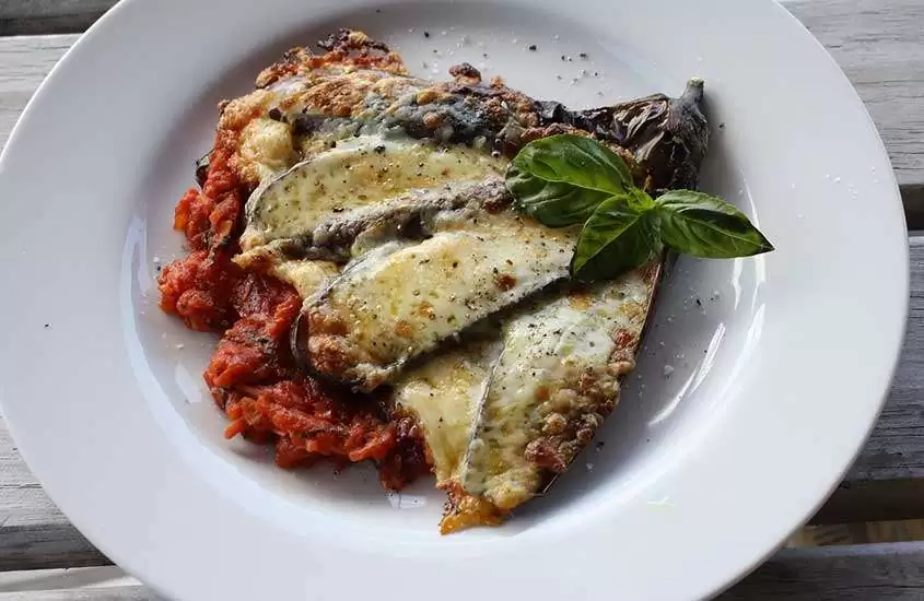vista de cima de lasanha vegetariana com fatias de berinjela empanadas, molho de tomate e queijo, uma das comidas típicas da itália, servida em prato redondo