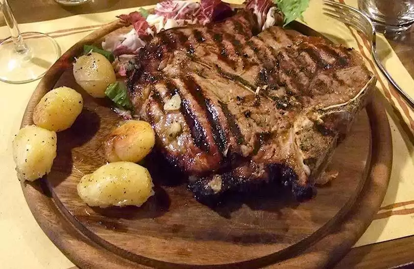 Pedaço suculento de bistecca alla Fiorentina, um tradicional e delicioso corte de carne italiana, servido em uma tábua redonda de madeira