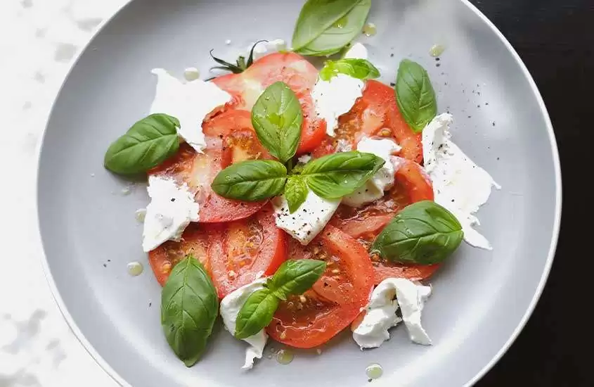 Vista aérea de uma deliciosa salada italiana, composta por tomate, mussarela fresca e manjericão, harmoniosamente servida em um prato redondo