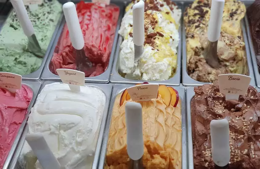 Vista superior de um congelador de sorveteria, repleto de diversos sabores de gelato, uma das sobremesas italianas