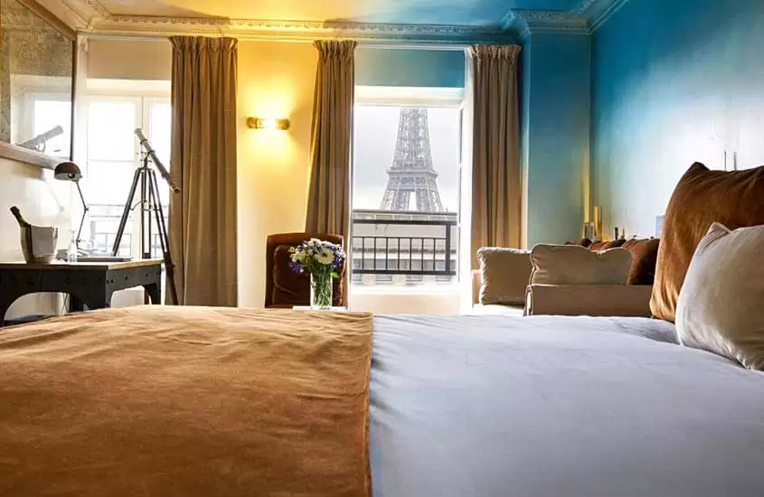 durante o dia, cama de casal, sofá e mesa em suíte de hotel em Paris com varanda e vista para Torre Eiffel
