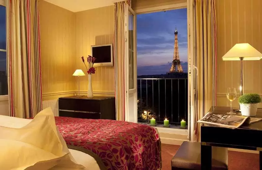 durante a noite, cama de casal e mesa em suíte com varanda e vista para a Torre Eiffel
