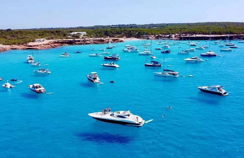 durante um dia ensolarado, barcos e iates em águas cristalinas de uma das praias de Ibiza.