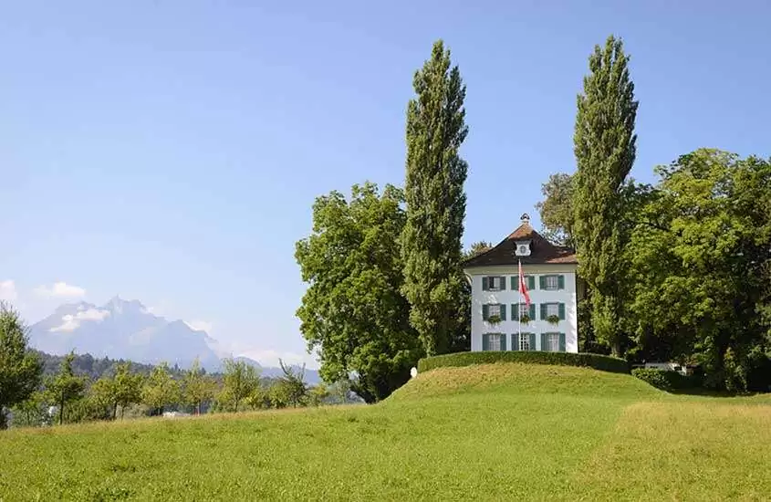 durante o dia, casa branca com 3 andares e telhado marrom, rodeada por árvores em montanha em Tribschen, um lugar onde ficar em Lucerna.