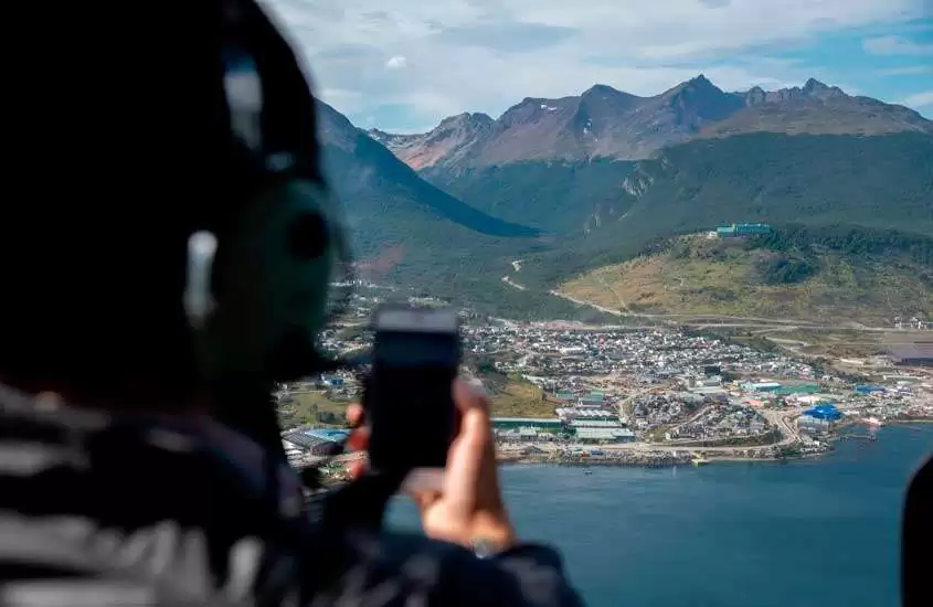 Pessoas tirando fotos da paisagem das montanhas, cidade e mar de Ushuaia, durante tour de helicóptero, um dos melhores passeios em ushuaia