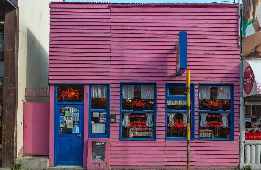 Durante o dia, loja com fachada rosa e detalhes azuis em ruas de Ushuaia